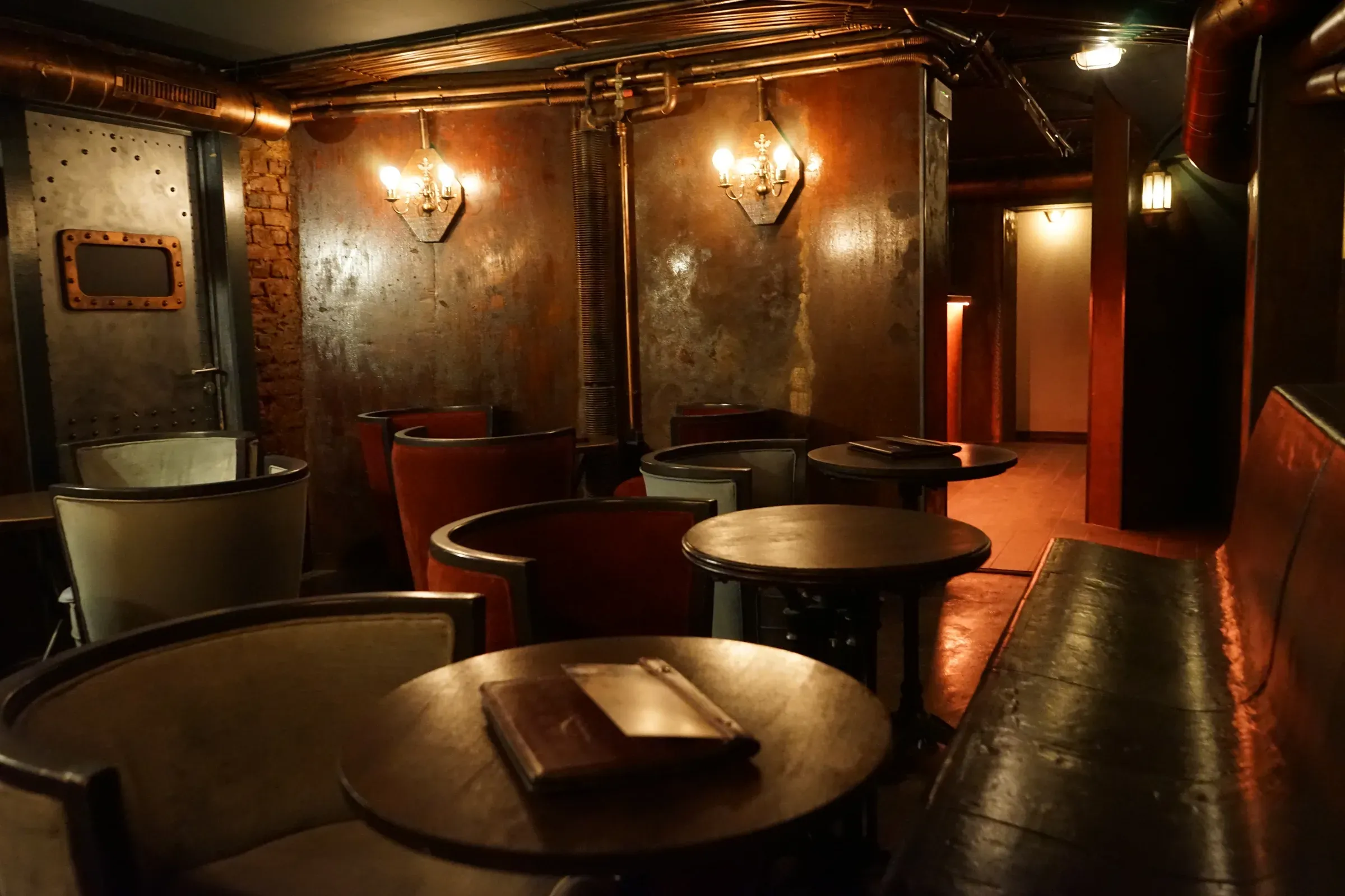 Fauteuils tonneau et tables rondes du Boudoir, sous les appliques et la tuyauterie de cuivre
