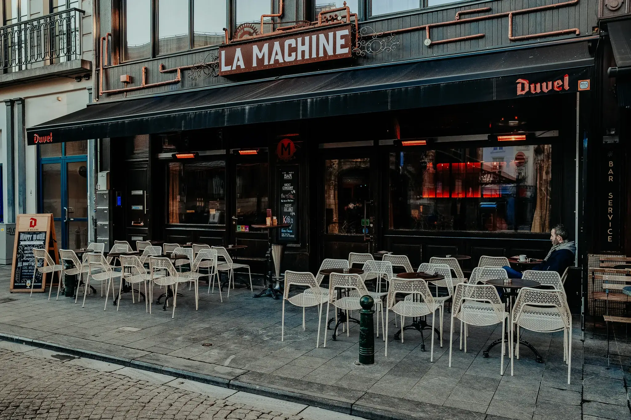 The front of La Machine on Place Saint-Géry: the red sign, the copper pipes and the terrace