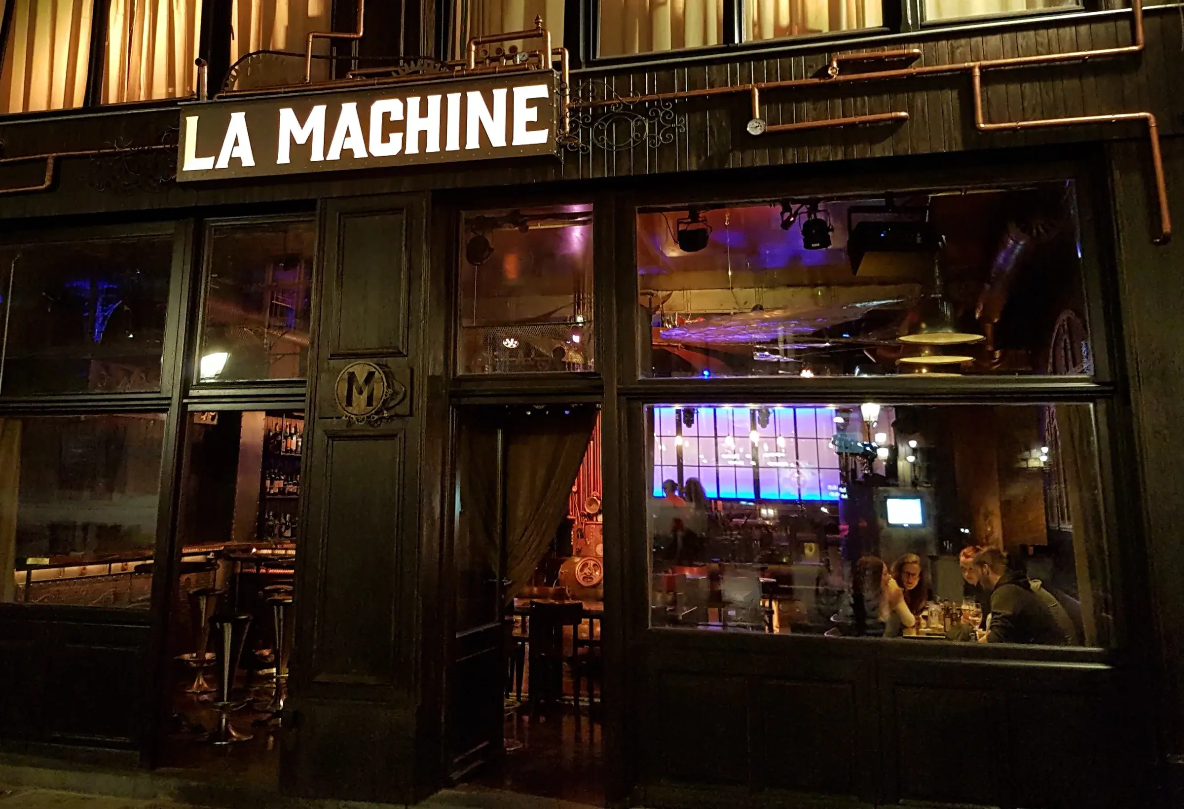 La Machine’s façade at night on Place Saint-Géry: the lit sign and the bar behind the windows
